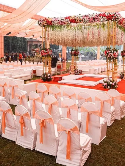 An elegant wedding mandap with peach-colored drapes and a canopy of hanging flowers. The clean and spacious seating arrangement ensures all guests have a clear view of the ceremony.