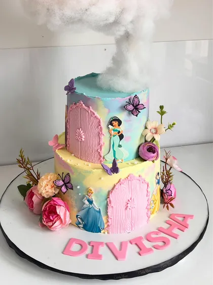 The bottom tier of the princess castle cake, featuring beloved characters like Cinderella and Jasmine, set against a pastel watercolor background with floral and butterfly accents.