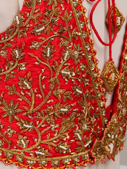This sleeveless red blouse is perfect for a bold bridal statement. It features a deep V-neckline and is heavily embellished with intricate gold floral zardozi work, creating a rich and luxurious feel.