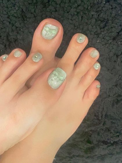 A fun and creative cat eye pedicure in a shimmery green shade with 3D bow accents.
