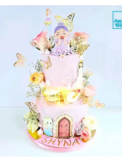 This is what I call a Princess Dream Cake. It's a three-tiered masterpiece with a fairy topper, fresh flowers, golden butterflies, and a castle door, creating a truly enchanting centerpiece for a royal celebration.