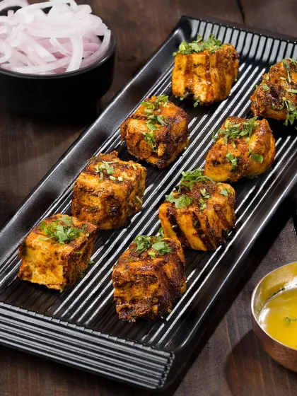 Cubes of paneer tikka arranged neatly on a modern black platter. This presentation is ideal for a restaurant menu, looking both delicious and professional.