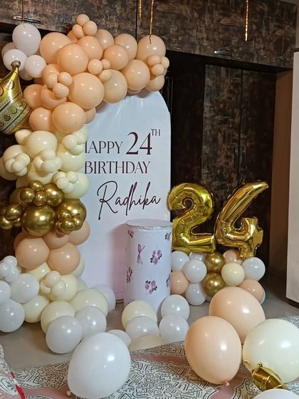 A close-up of the personalized backdrop for Radhika's 24th birthday, showing the details of the balloon garland with a gold crown foil balloon and number balloons.