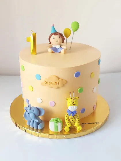 A delicate pastel cake for a first birthday, featuring a fondant girl topper and her favorite animals, an elephant and a giraffe.