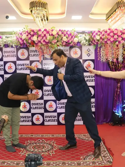 A light-hearted moment on stage where a student seeks blessings from his teachers in a fun way.