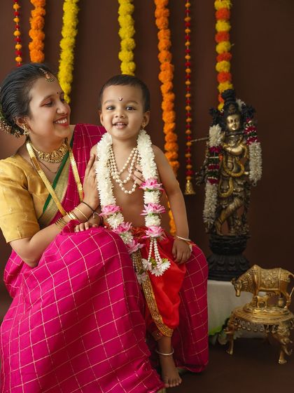 A sweet moment where the mother looks lovingly at her son, who is dressed as little Krishna and smiling for the camera.