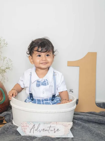 A proud one-year-old boy in his adventure-themed photoshoot. Sitting in a bucket with a large number '1' prop, he is ready to celebrate his big milestone.