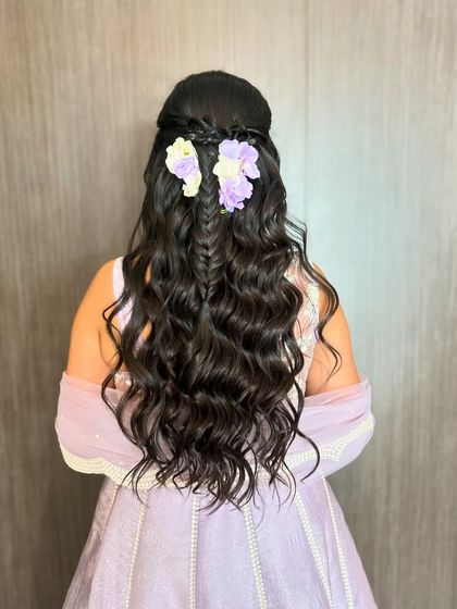 A beautiful half-up style with a central fishtail braid, soft waves, and lavender flowers, perfect for a Haldi or Mehendi.