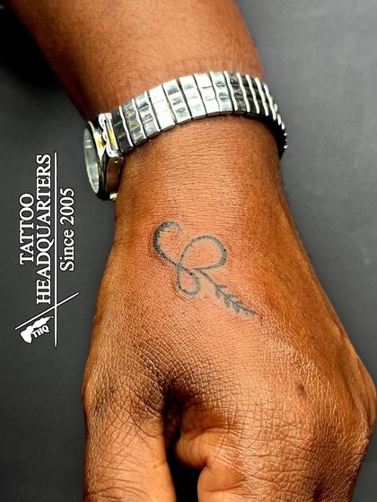 A small initial 'R' combined with a leaf design, tattooed on the hand.