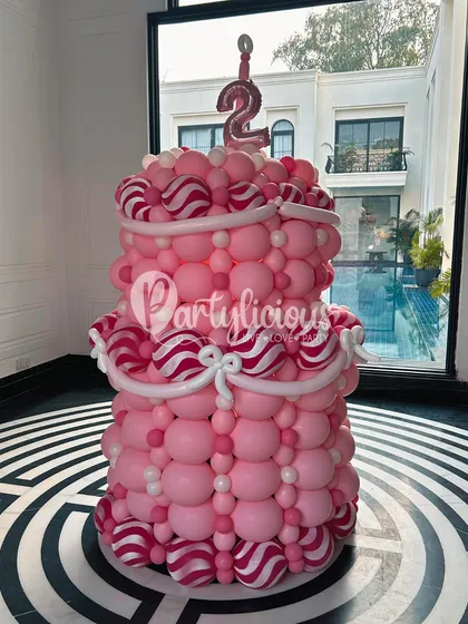 You can't have a birthday party without a cake! This two-tiered birthday cake sculpture, complete with candy-striped details and a number '2' candle, is a fun and calorie-free centerpiece.