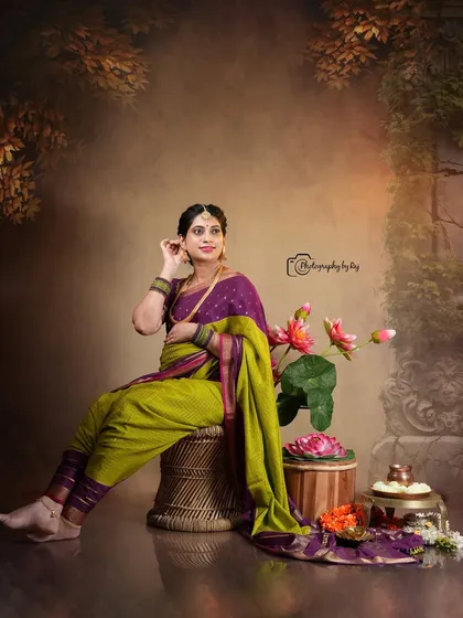 An artistic studio portrait of a mother-to-be in a traditional nauvari saree, seated with lotus flower props.