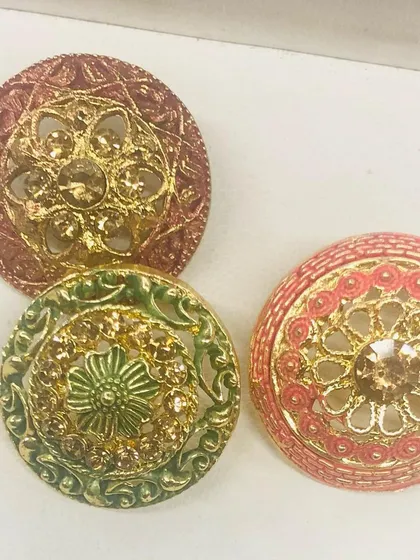 Detailed and ornate, these metal buttons showcase intricate filigree work with a central crystal. The designs are available in rustic gold, green, and pink tones, suitable for festive and wedding attire.
