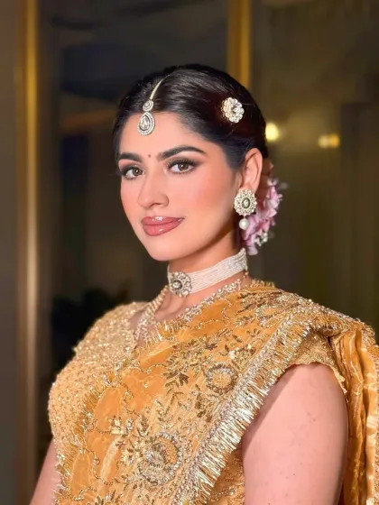 A close-up of the bride's soft, glamorous makeup and jewelry. The styling is designed to enhance her natural beauty and complement the golden ensemble.