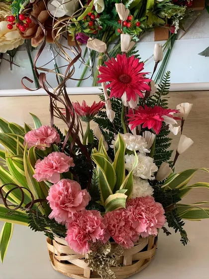 A lovely basket arrangement of fresh pink carnations, white carnations, and red gerbera daisies. The natural woven basket gives it a charming, rustic feel.