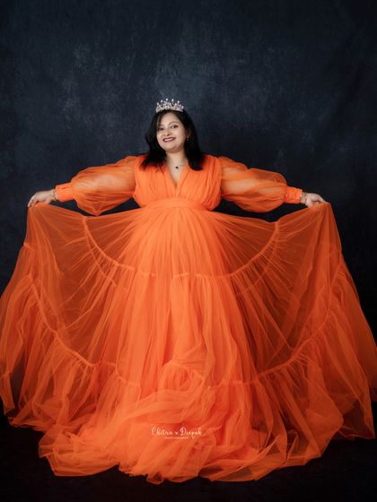 A happy princess moment. This mom-to-be is all smiles in a vibrant orange gown and tiara, holding out the full skirt of her dress.