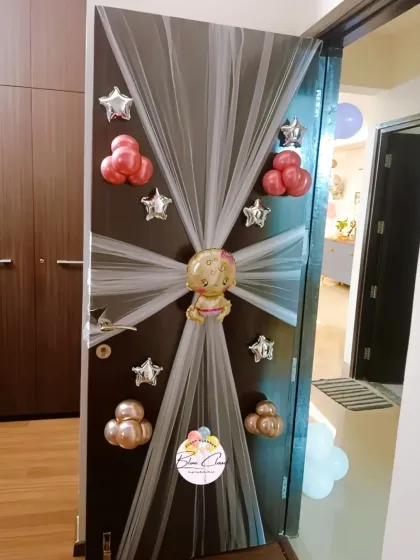 A charming door decoration to welcome a new baby, using white netting and pink and silver foil balloons.