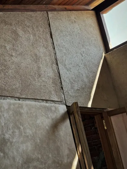 Sunlight streams into a room, highlighting the subtle texture of the lime plaster walls. The angled ceiling and clerestory window are designed to bring in natural light while maintaining a sense of enclosure.