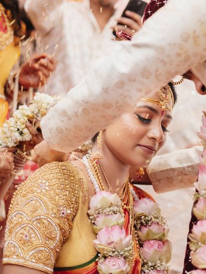 A close-up of the 'akshata' ceremony, where rice grains are showered on the bride as a blessing. The focus is on her serene expression and the fine details of the moment.