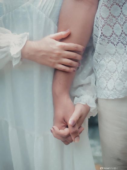 A close-up detail shot of the couple holding hands by the waterfall. This image focuses on their intertwined fingers, symbolizing their strong and steady bond.