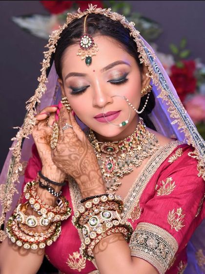A beautiful bride in a pinkish-red lehenga, adorned with heavy kundan and pearl jewellery.