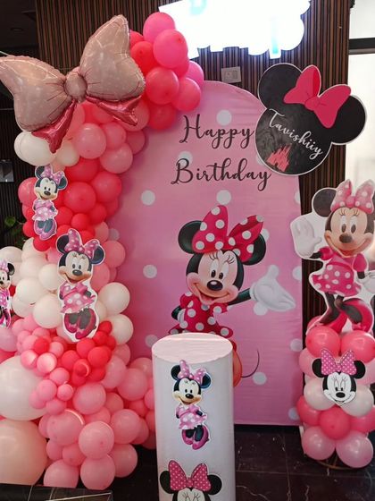 A classic Minnie Mouse theme party in shades of pink and white, featuring character cutouts, a polka-dot backdrop, and a large bow foil balloon.