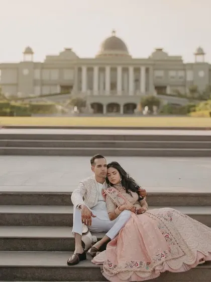 A grand portrait on the steps of a modern palace. This shot captures the scale of the venue and the elegance of the couple, creating a picture-perfect memory from their Mehendi ceremony.