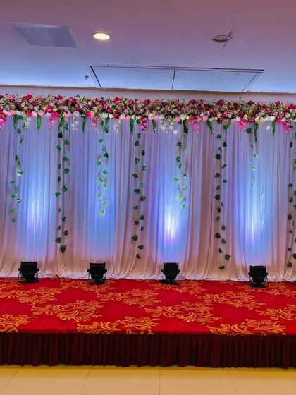 A simple and elegant stage backdrop with white drapes and hanging green vines. The uplighting adds a touch of drama and sophistication.