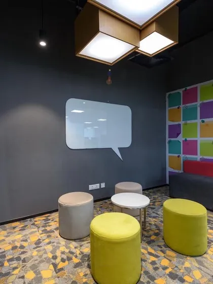 An "ideation corner" with a speech-bubble-shaped whiteboard and colorful poufs for seating. The wall features a graphic of colorful sticky notes, encouraging brainstorming.