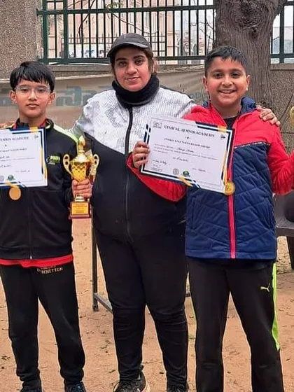 Two young boys from our academy proudly display their trophies and certificates alongside their coach. These wins at the Ideal Tennis Open and Saket Ethical Open highlight the success of our junior program.