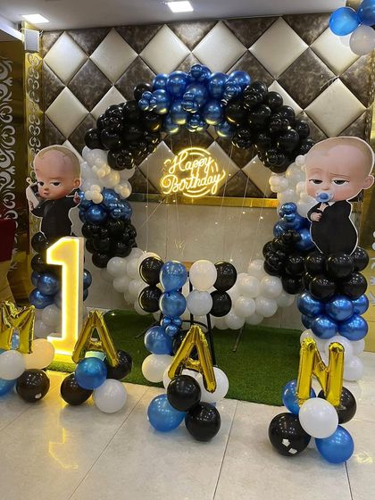 This is a duplicate of ID 30, 95, 220, 248, 253. A classic Boss Baby theme for a first birthday. This setup includes a balloon arch in blue, black, and white, character cutouts, a 'Happy Birthday' neon sign, and a light-up number '1'.