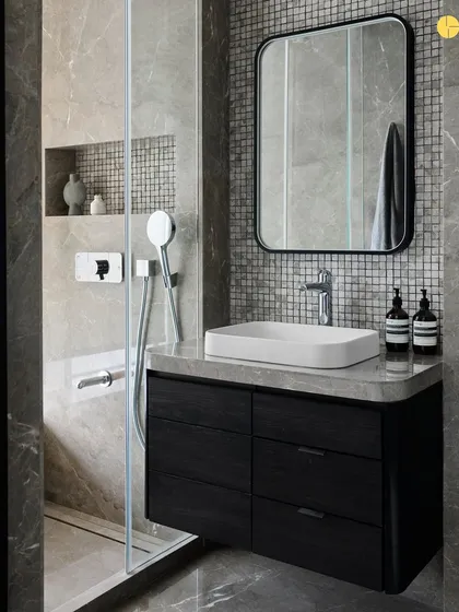 A modern bathroom design from 'Pad by the Bay.' The space uses dark wood for the vanity and mosaic tiles for the shower wall, creating a sophisticated and moody atmosphere. The clean lines of the sink and faucet add to the contemporary feel.