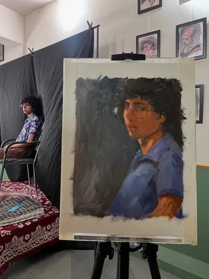 The portrait of Ember on the easel, with the model sitting in the background. This image gives a sense of the studio environment and the setup for a live alla prima painting session.