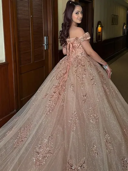 A back view of a client in a sparkling rose gold ball gown. The long train and lace-up back create a stunning silhouette, perfect for photos.
