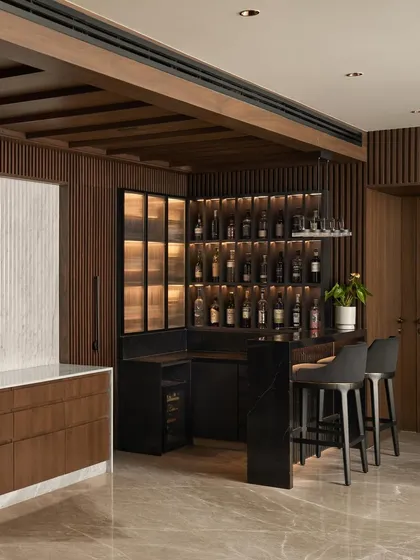 This bar area was custom designed with a black marble counter, backlit bottle display, and integrated wine cooler. The fluted wood paneling and frosted glass cabinets tie it into the home's overall aesthetic of warm, modern luxury.
