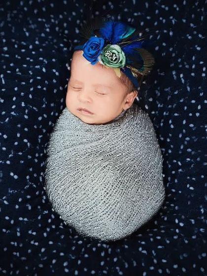 A sleeping newborn girl with a beautiful blue and green floral headband. The colors pop against the dark, starry background, creating a stunning portrait.
