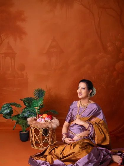 A hopeful and serene portrait. The mom-to-be, dressed in a traditional saree, looks upward with a gentle smile, surrounded by an artistic, painted landscape.