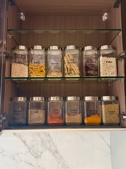 A cabinet showcasing a variety of pantry staples, including pasta, poha, and spices, all stored in matching glass jars. This uniform look brings a sense of calm and order to the kitchen.