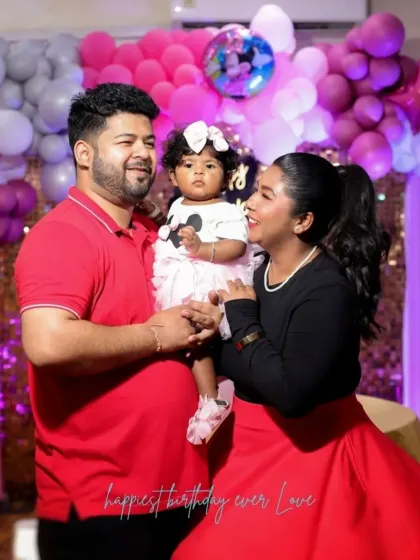 A happy family of three posing for a photo during a birthday celebration. The pink and silver balloon decor adds a festive touch to this family portrait.
