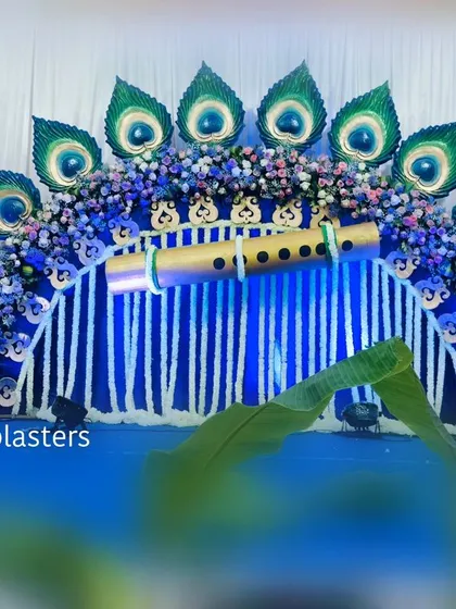 A divine Krishna-themed naming ceremony. The centerpiece is a stunning backdrop of peacock feathers and a golden flute, created with a mix of fresh flowers and custom props, all set against a vibrant blue that is symbolic of Lord Krishna.