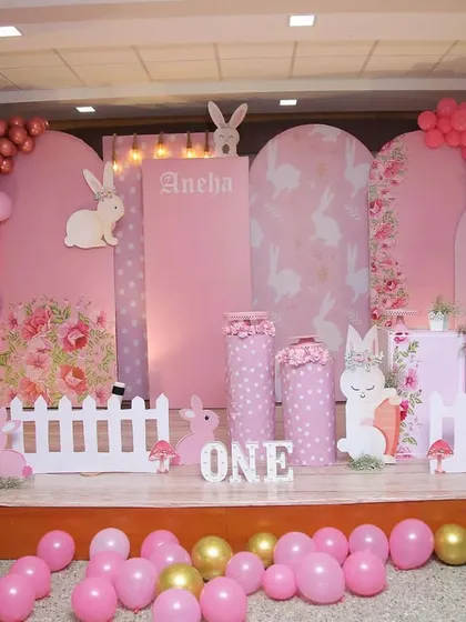 A sweet bunny-themed party with a pink and gold color palette. The stage features bunny cutouts, a picket fence, and beautiful floral-patterned backdrops.