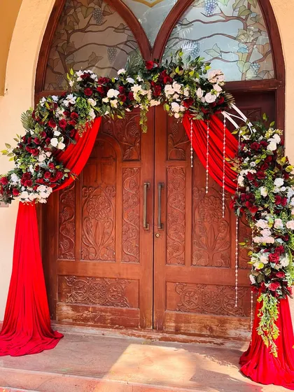 A classic and dramatic entrance for a church wedding. This floral arch combines rich red draping with maroon and white roses, creating a grand and welcoming entryway for the couple and their guests.