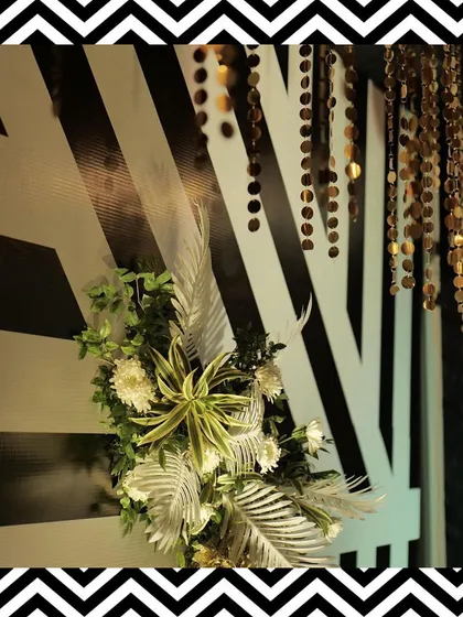 Decor details from the black and white theme, featuring golden sequin hangings and tropical leaves against a striped backdrop.