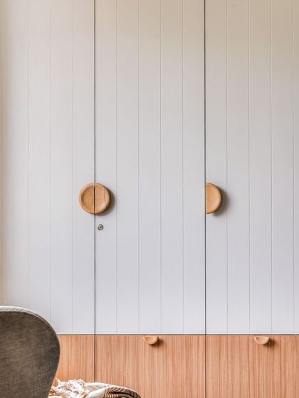 This master wardrobe continues the home's transitional design language, featuring sleek white grooved shutters with natural wood accents and custom circular wooden handles.