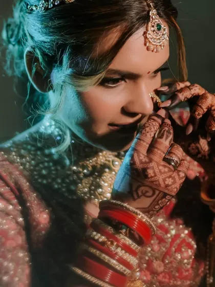 A close-up of the bride adjusting her nose ring. This intimate shot highlights the beautiful henna on her hands and the delicate details of her bridal jewelry.