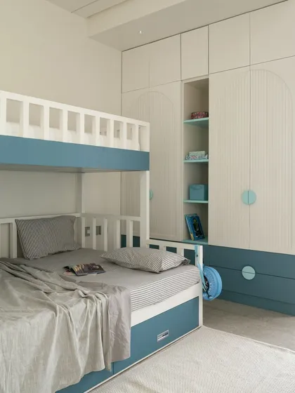 For this children's room, I designed a custom bunk bed and wardrobe combination to maximize space and fun. The calming blue and white palette, along with arched details and integrated shelving, creates a functional sanctuary for play, study, and rest.