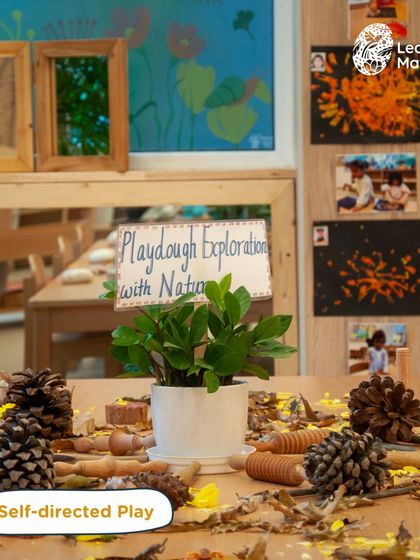 An invitation for self-directed play using natural materials. Pinecones, wood slices, and autumn leaves are arranged on a table, waiting for children to transform them into a forest, a creature, or a story.