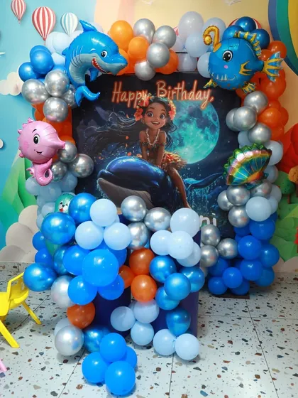 A Moana-themed "Under the Sea" party setup, with a beautiful backdrop of Moana and a vibrant balloon arch featuring friendly sea creatures.