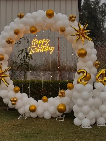 An outdoor balloon ring in white and gold with starburst accents for a 24th birthday.