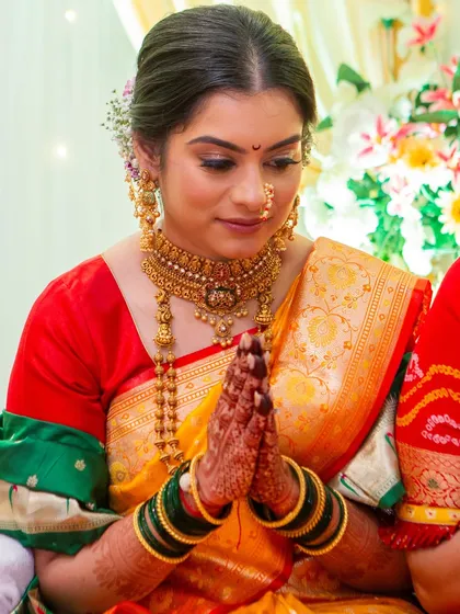 A candid moment of a Maharashtrian bride during her ceremony. The makeup is kept soft and radiant with golden hues to match her jewelry, and the hair is styled in a traditional updo with fresh flowers.