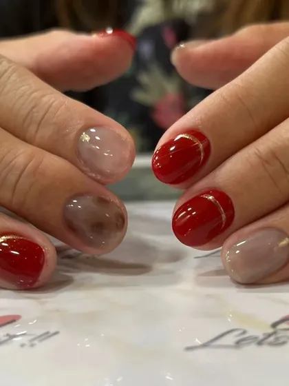 A sophisticated manicure combining glossy red nails with smoky, marbled accent nails and a delicate gold stripe.